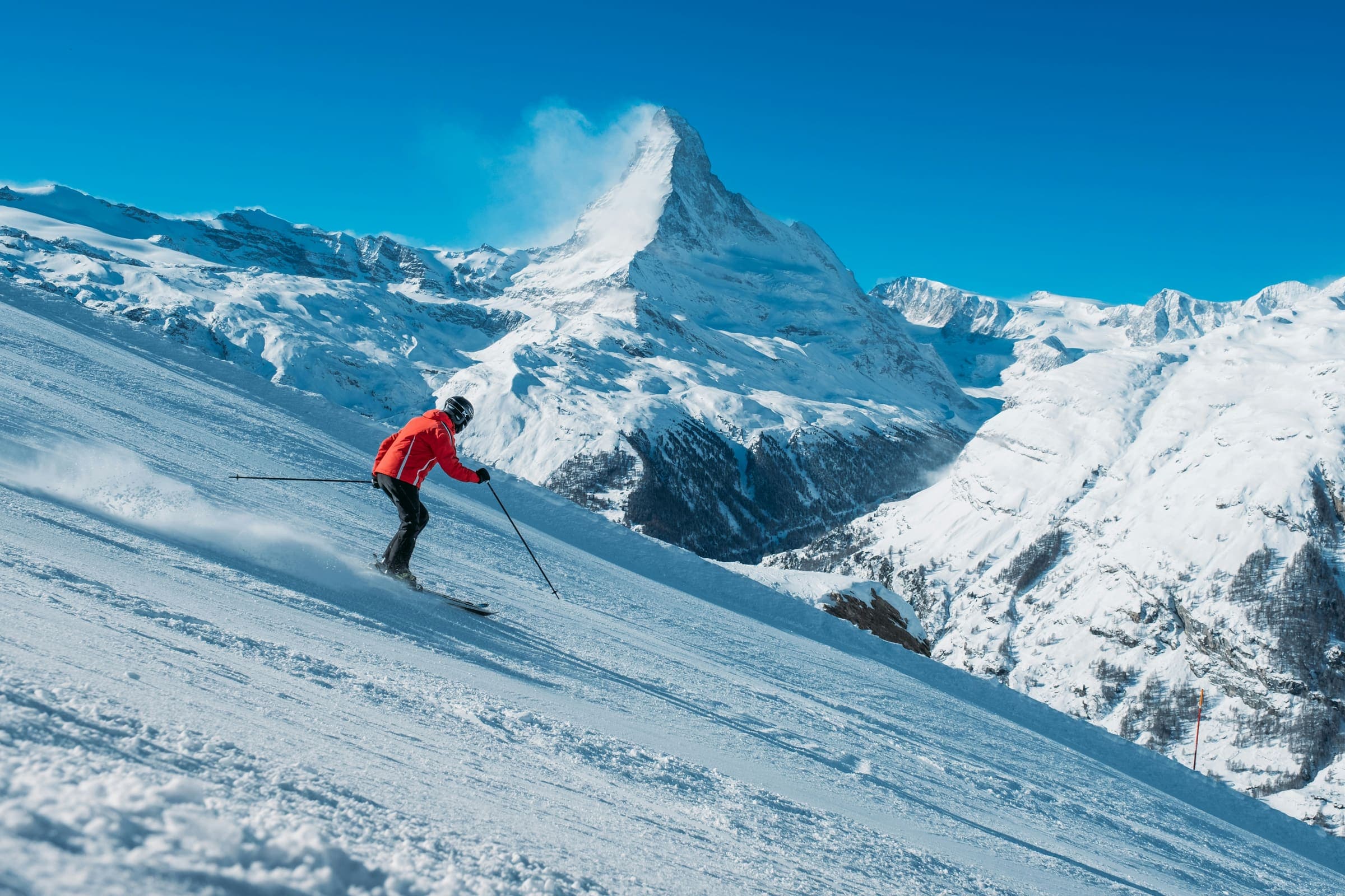 Skiër in een rode jas op de piste, met de Matterhorn op de achtergrond